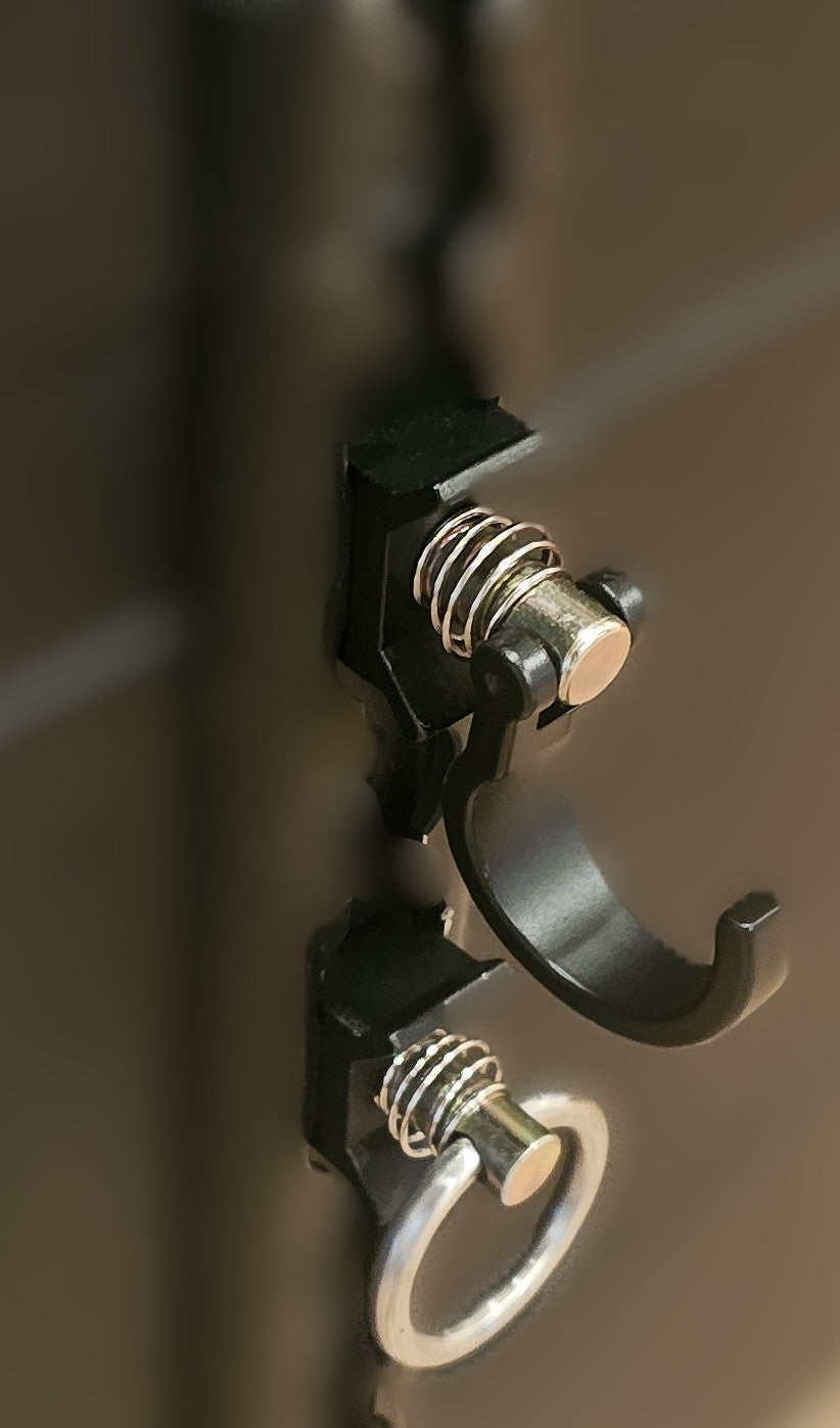Paradox Aviation cargo track accessories including a black spring-loaded hook and metal ring on a dark case surface